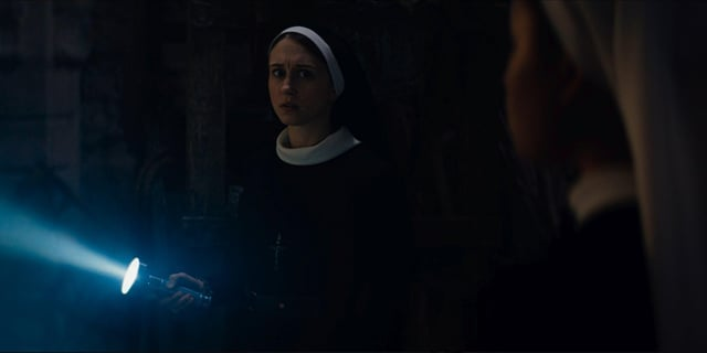 Hermana Irene, personaje de la película "La Monja 2" sosteniendo una linterna en un lugar oscuro. 