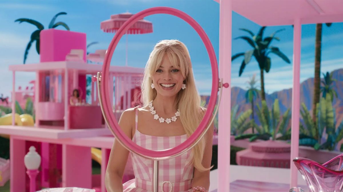 Margot Robbie actuando como Barbie. Barbie está sentada en su tocador de color rosa y se mira sonriendo en un espejo sin vidrio.
