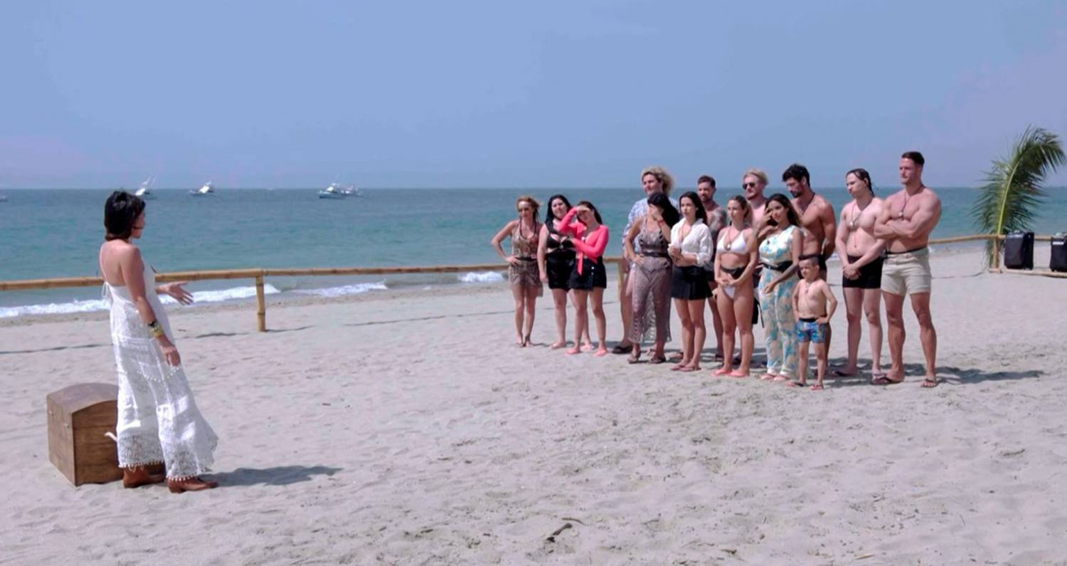 El cast completo de Tierra Brava en traje de baño en un fila sobre la arena, escuchando las instrucciones de la animadora Karla Constant.