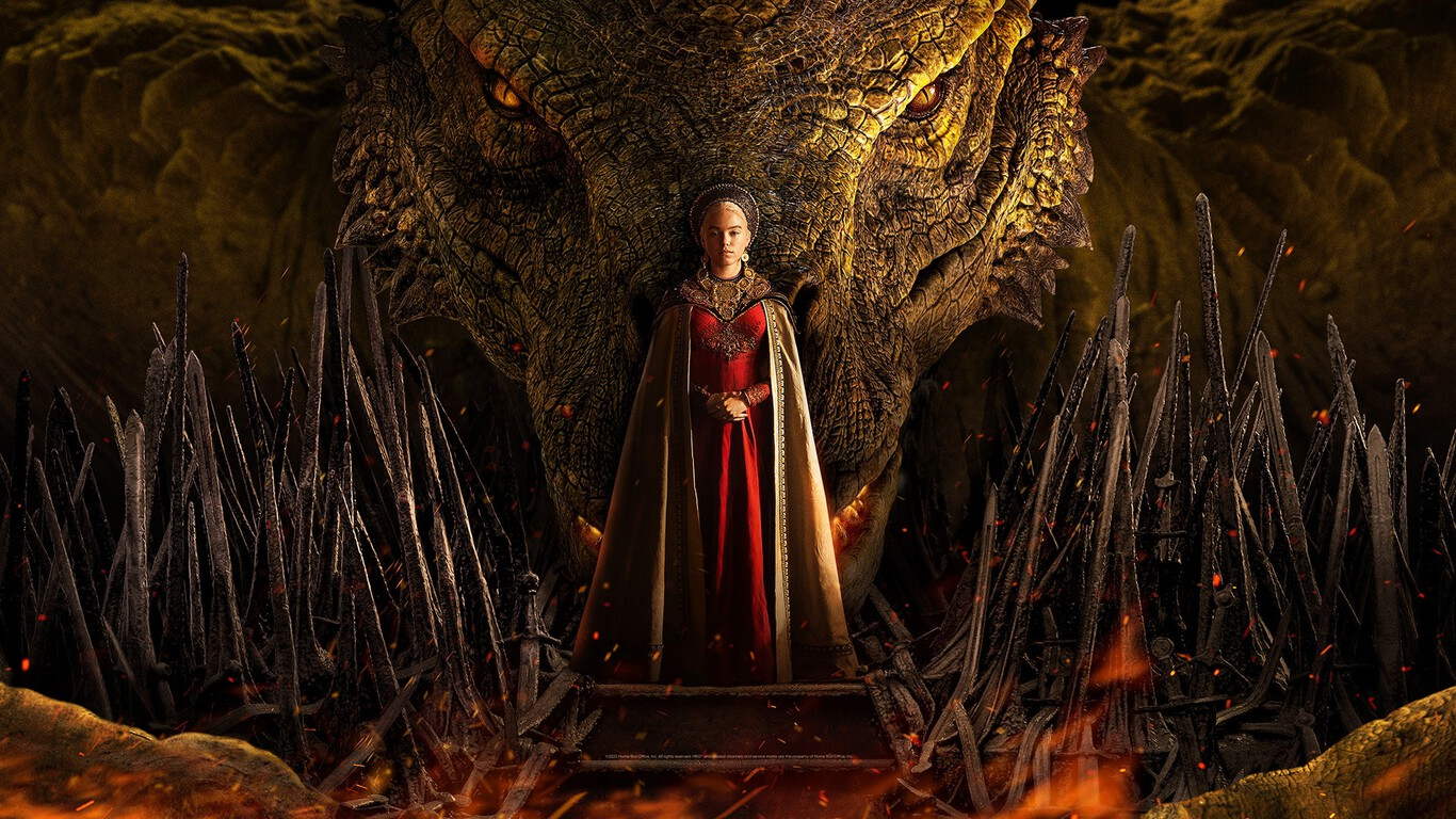 Emilia Clarke interpretando a Daenerys Targaryen en La Casa del Dragón. Mujer de la realiza con un vestido rojo y capa dorada y diadema. Parada al centro rodeada de espadas y de fondo el rostro de un dragón. Imponente mira a la cámara con las manos entrelazadas.