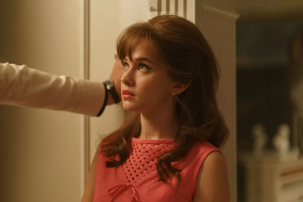 Cailee Spaeny interpretando a Priscilla Beaulieu. Ella está apoyada en una pared, mirando a un personaje fuera de cámara en una ambientación dentro de una casa.