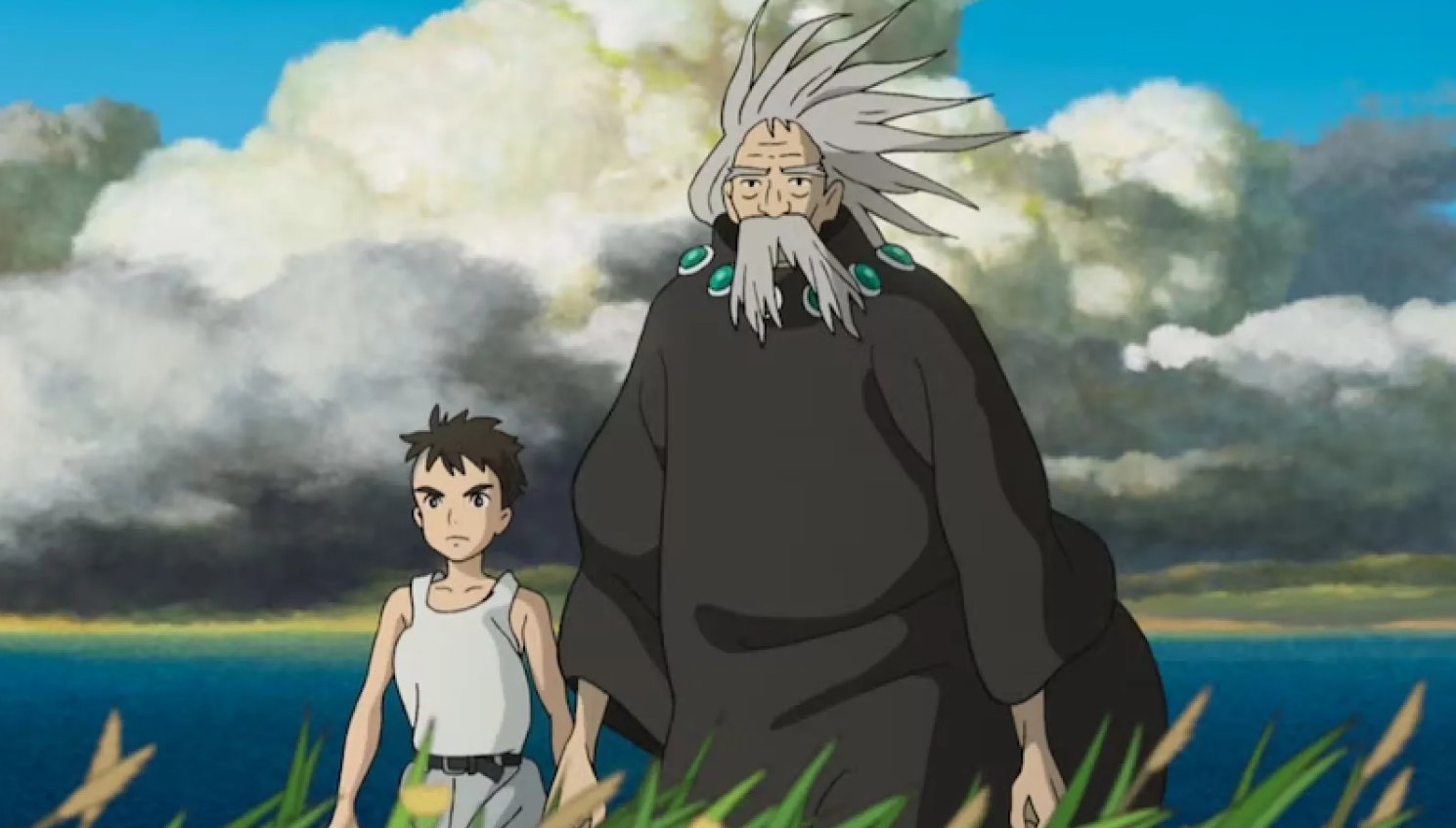 Mahito Maki, un niño de 12 años junto a su tío abuelo en un plano general parados sobre el pasto, con el mar de fondo y grandes nubes blancas y grises sobre ellos. 