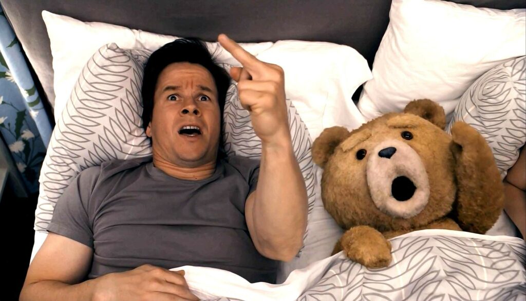 John Bennett y el oso Ted acostados levantando el dedo medio